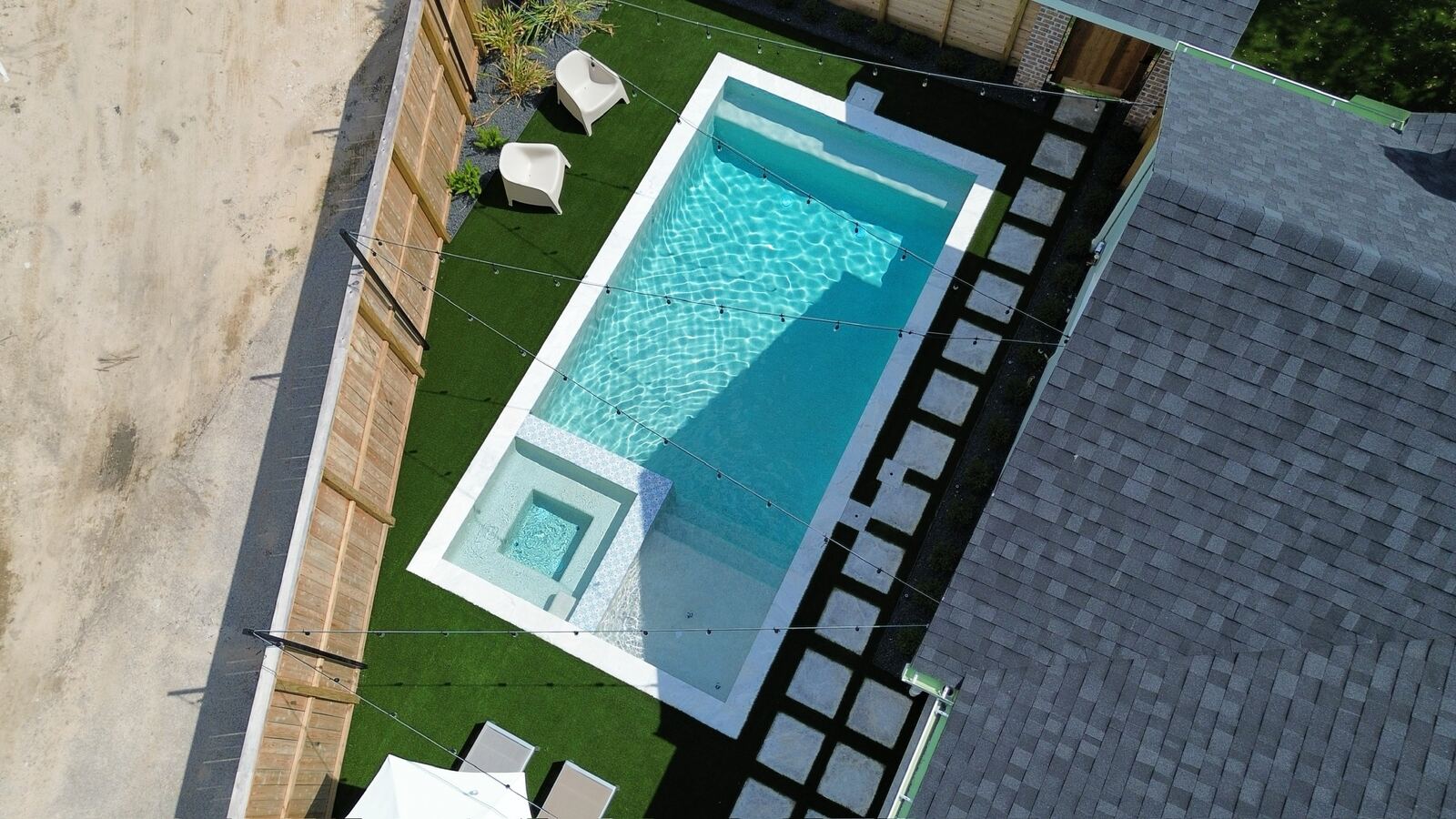 Aerial view of a small pool with hot tub, turf and string lights