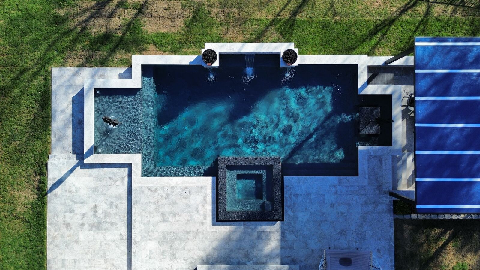 Aerial view of a cross-shaped pool with fire pit and lounge seating