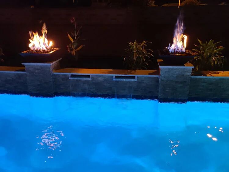 Nighttime pool with fire bowls and a stacked-stone raised wall