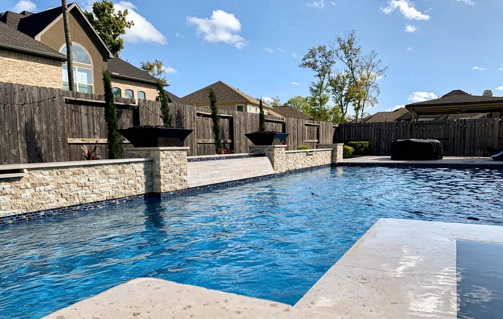 Pool with raised fire bowls, stacked-stone wall and string lights