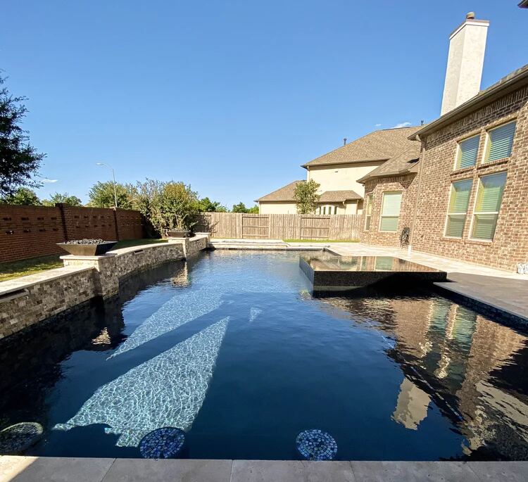Dark-finish pool with raised tanning ledge beside a brick home