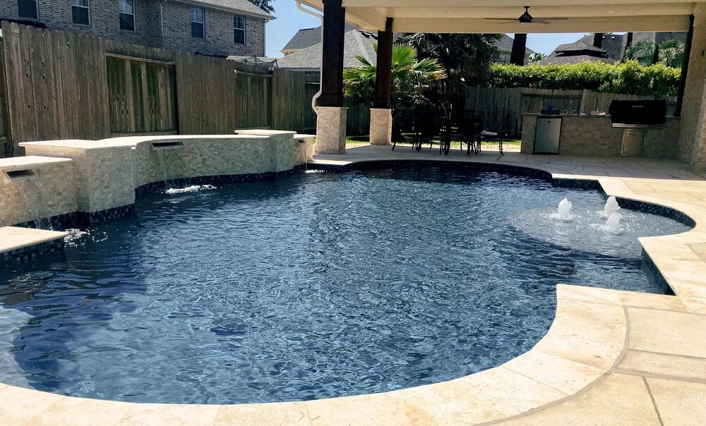 Pool with raised spa waterfall beside a covered outdoor kitchen