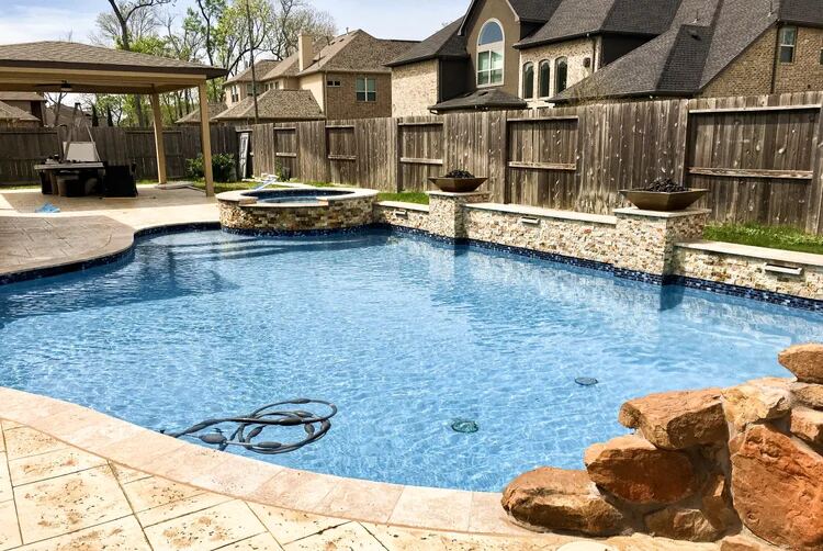 Covered outdoor kitchen beside a freeform pool with bubblers