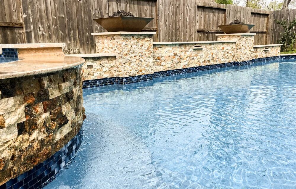 Stacked-stone raised wall with fire bowls and blue tile waterline