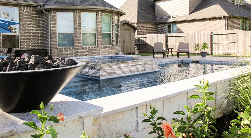 Pool reflecting trees beside a raised wall with fire bowls