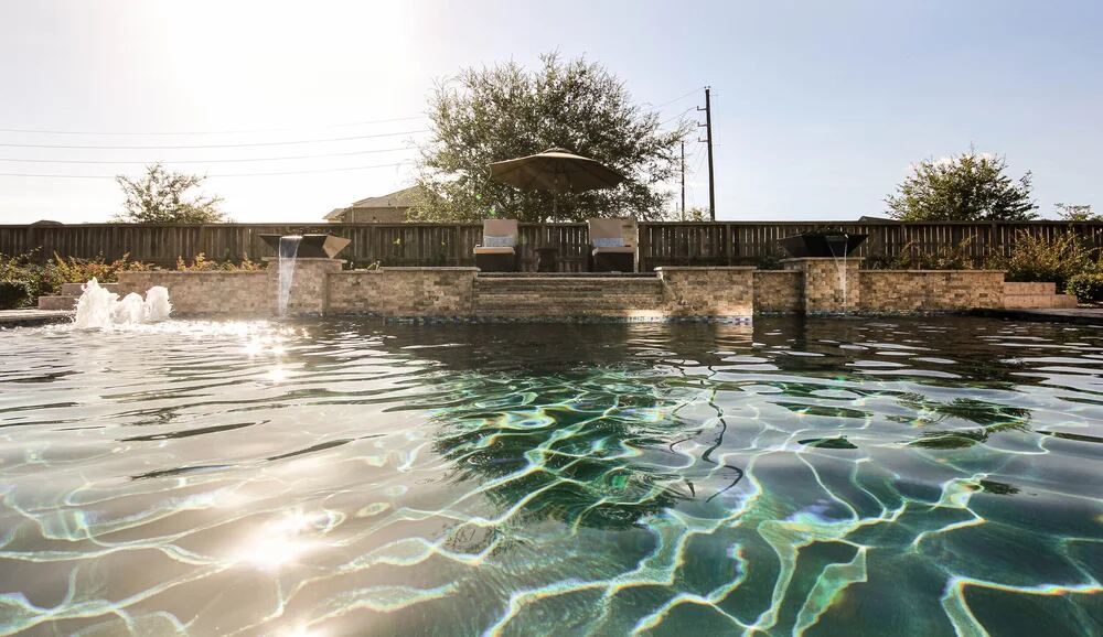 Sunlit pool surface beside a waterfall wall and patio seating