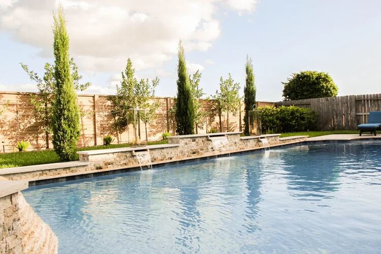Pool beneath cypress trees with a stacked-stone spillway wall