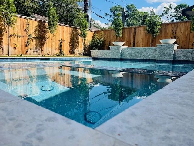 Pool with in-water tanning ledge bubblers beside a stacked-stone wall