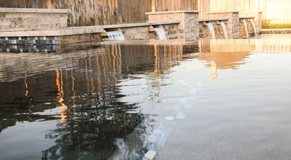 Row of waterfall spillways along a stone wall with reflections